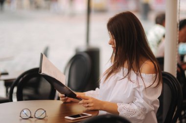 Şık Bayan merkezinin şehir ve menüsüne göz kafede oturuyor. Güneşli havalarda ve codl iç. Güneş gözlüklü kız ne sipariş için seçer