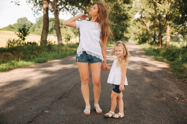 Matka a malá dcerka chodit když uličkou a navzájem ruce — Stock fotografie