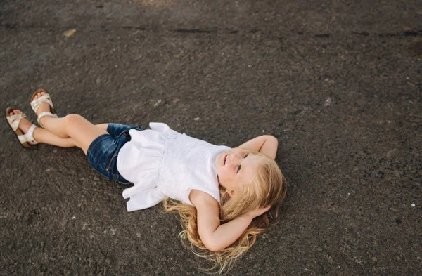 Petite fille allongée sur la route près de la grande ruelle — Photo