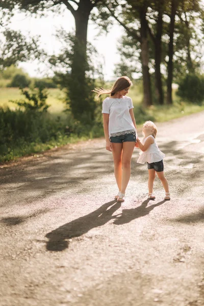 Η μητέρα και η μικρή κόρη του αν και περπατήστε το δρομάκι και κρατήστε τα χέρια κάθε τους άλλους. Σκιά στο δρόμο — Φωτογραφία Αρχείου