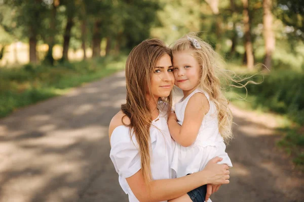 O familie iubitoare fericită. Mama şi fiica ei se joacă şi se îmbrăţişează. alee de copaci mari — Fotografie, imagine de stoc