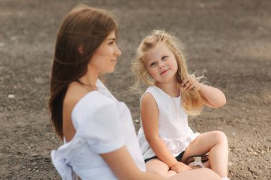Çekici anne ve sarı saçlı kızı oturur büyük sokak yakınındaki yolda. Gülümse ve natune için görün