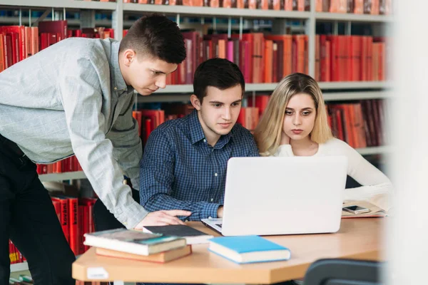 Estudiantes universitarios sentados juntos en la mesa con libros y laptop. Jóvenes felices haciendo estudios en grupo en la biblioteca — Foto de Stock