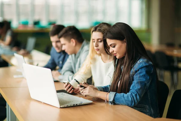 Группа студентов колледжа, обучающихся в школьной библиотеке, девочка и мальчик пользуются ноутбуком и подключаются к интернету — стоковое фото