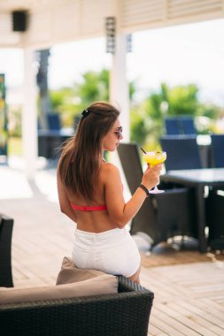 Çekici kız plaj bar üzerinde dinlenme ferahlatıcı bir kokteyl içki. Parlak mayolar ve güneş gözlüğü