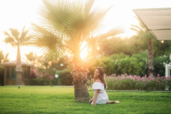 Hermosa morena sentada en la hierba cerca de la palma —  Fotos de Stock