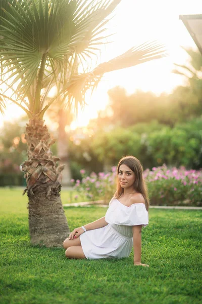 Schöne Brünette sitzt auf Gras in der Nähe der Palme — Stockfoto