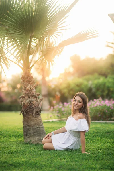 Schöne Brünette sitzt auf Gras in der Nähe der Palme — Stockfoto