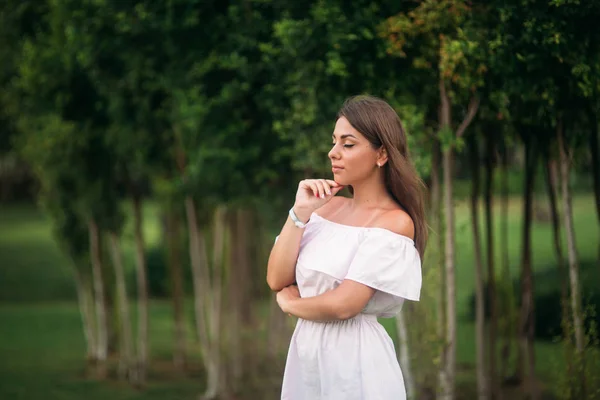 Chica joven y bonita en una ciudad de verano de pie cerca del árbol —  Fotos de Stock