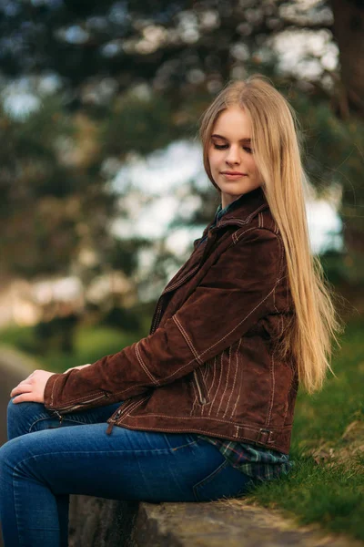 Una bella ragazza sta camminando lungo l'argine. Capelli biondi e giacca marrone. Primavera — Foto Stock