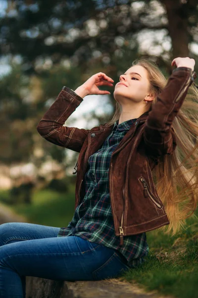 Una hermosa chica está caminando por el terraplén. Cabello rubio y chaqueta marrón. Primavera —  Fotos de Stock