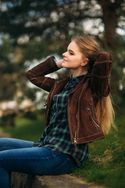 Una hermosa chica está caminando por el terraplén. Cabello rubio y chaqueta marrón. Primavera —  Fotos de Stock