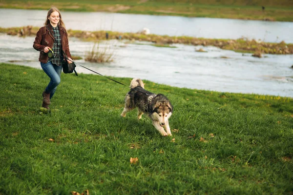Bir kız ile bir köpek set boyunca yürüyor. Güzel Husky köpek. Nehir. Bahar