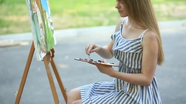 Девушка-художник стоит на табуретке в парке и держит палитру с пайетками — стоковое видео