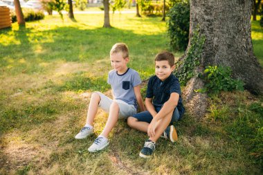 İki erkek tree yakınındaki çimlerin üzerine oturur. Sekiz yıl eski çocuk parkta vakit