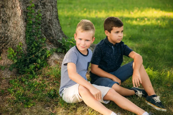 Two boys sits on grass near the tree. Eight year old children spend time in park — Stock Photo, Image