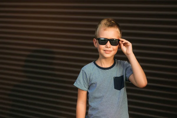 Gutaussehender Junge lächelt und posiert für den Fotografen. Junge hat Sonnenbrille — Stockfoto