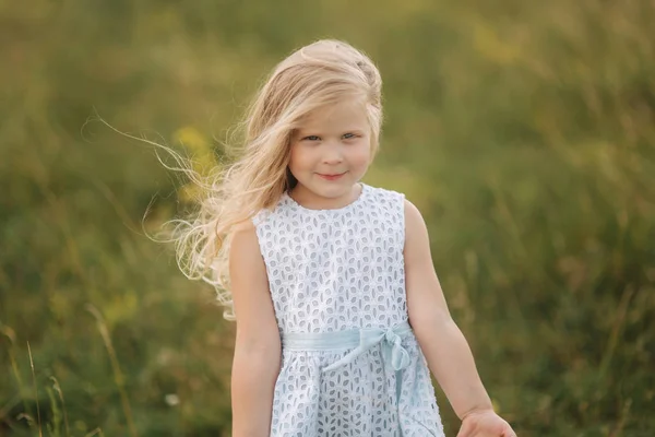Klein meisje in hemelsblauw jurk staan in het veld voor grote boom — Stockfoto