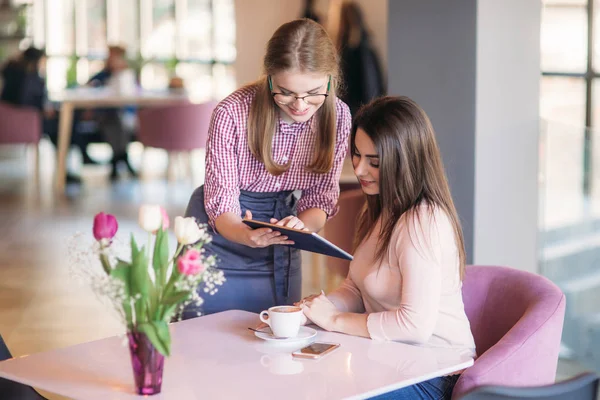 Привлекательная молодая официантка с помощью планшетного компьютера принимает заказ от клиента в кофейне — стоковое фото