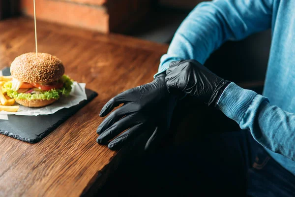 Hombre con guantes negros toma una hamburguesa en sus manos — Foto de Stock