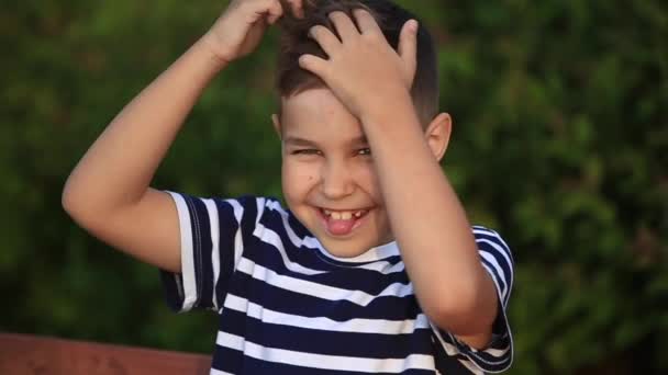 Un niño pequeño con una camiseta a rayas sonríe y se alegra. — Vídeos de Stock