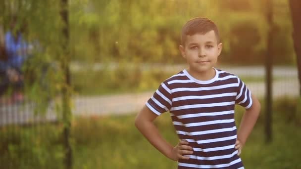 Un niño pequeño con una camiseta a rayas sonríe y se alegra. — Vídeos de Stock