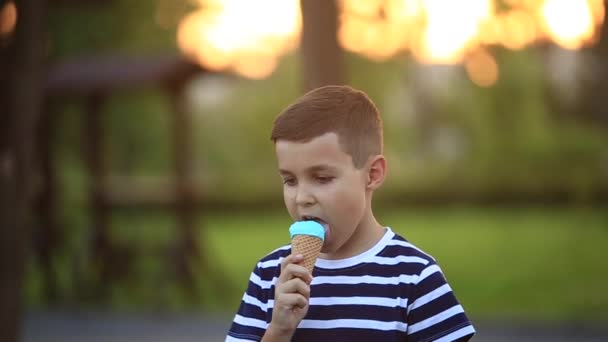Маленький хлопчик у смугастій футболці їсть блакитне морозиво. Весна, сонячна погода — стокове відео