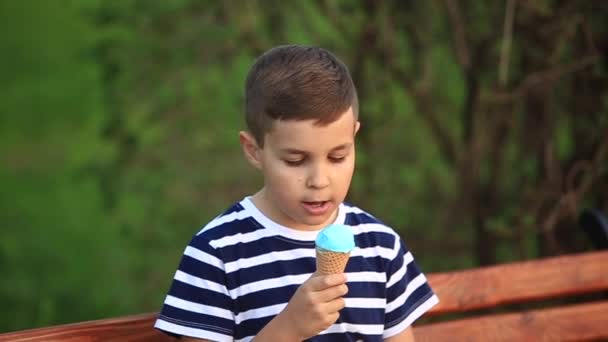 En liten pojke i en randig T-shirt äta blå glass. Våren, soligt väder — Stockvideo