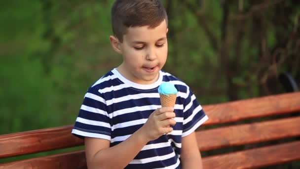 Um menino em uma camiseta listrada está comendo sorvete azul.Primavera, tempo ensolarado — Vídeo de Stock