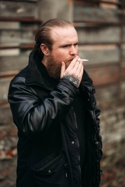 Siyah deri ceketli sakallı bir adam dışında anlamına gelir ve bir fotoğrafçı için poz veriyor. Sigara sigaret