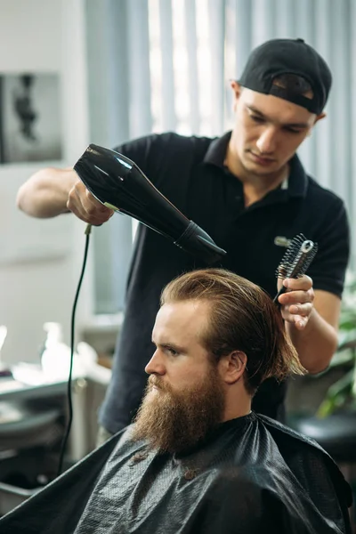 Mester csökkenti a haj és a szakáll, a férfiak a fodrászatban, és használ egy hajszárító — Stock Fotó