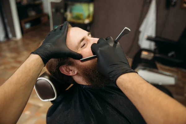 Бородатый мужчина с длинной бородой, стильное бритье, стрижка, с бритвой парикмахера в парикмахерской — стоковое фото