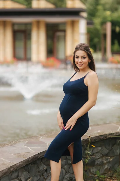 Красива молода весела вагітна жінка, що стоїть на фоні фонтану — стокове фото