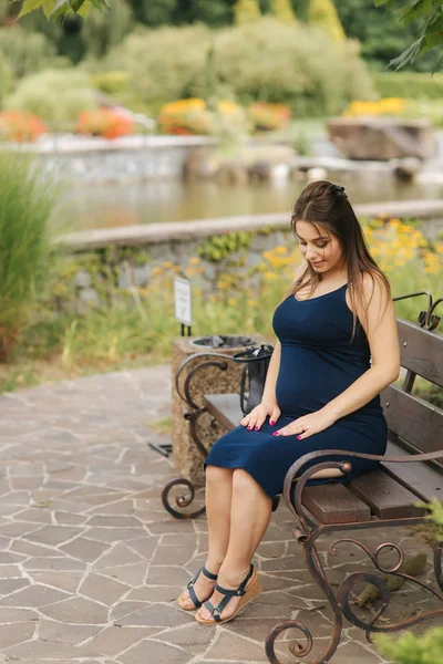 Mujer embarazada sentada en un banco cerca del lago — Foto de Stock