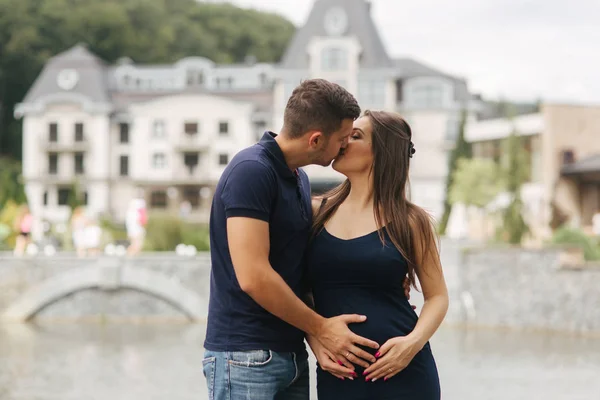Беременная женщина целует мужа, а он держит его руку на животе. — стоковое фото