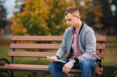 Sevimli öğrenci bankta oturur ve bir pensil kullanarak onun notebool onun düşüncelerinde aşağı yazıyor. dışında çalışma