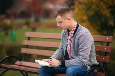 Sevimli öğrenci bankta oturur ve bir pensil kullanarak onun notebool onun düşüncelerinde aşağı yazıyor. dışında çalışma