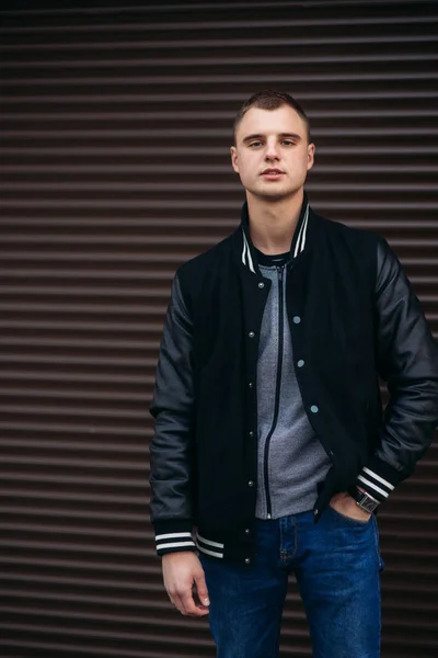Un joven con una chaqueta negra sobre un fondo de pared de rayas oscuras — Foto de Stock