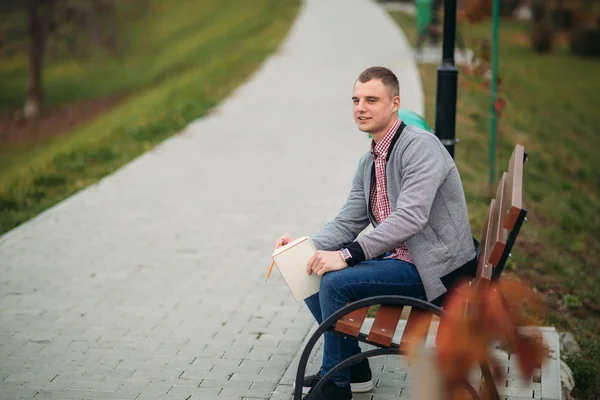 Χαριτωμένο φοιτητής κάθεται στον πάγκο και γράφει κάτω τις σκέψεις του για τον οποίο χρησιμοποιώντας ένα pensil. σπουδές εξωτερικό — Φωτογραφία Αρχείου