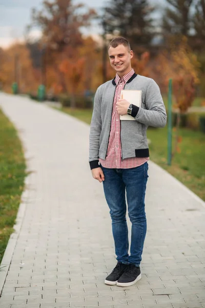 Estudiante divertido con cuaderno. Guy se para en el parque y sonríe — Foto de Stock
