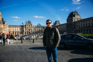 Bir genç adam turist haki ceket Louvre arka plan üzerinde duruyor. Güneşli sonbahar hava