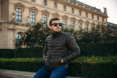 Yakışıklı adam haki bir ceket ve güneş gözlüğü bard üzerinde oturuyor. Adam gülümseme ve dinlen. tourits