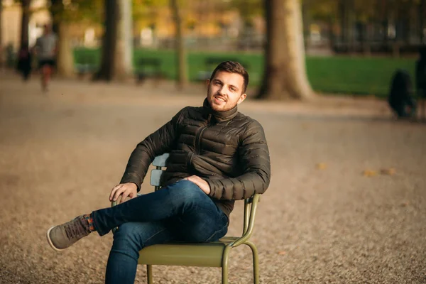 Un bel homme est assis au milieu du parc dans des tabourets kaki — Photo