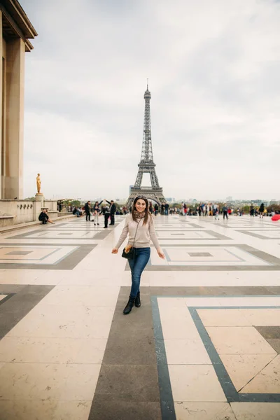 Menina bonita posando para o fotógrafo contra o fundo da Torre Eiffel. Fotosessão de Outono. Tempo ensolarado. Belo sorriso e maquiagem — Fotografia de Stock