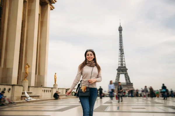 Hermosa chica posando ante el fotógrafo sobre el fondo de la Torre Eiffel. Fotosesión de otoño. Clima soleado. Hermosa sonrisa y maquillaje —  Fotos de Stock