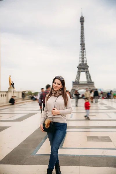 Красивая девушка позирует фотографу на фоне Эйфелевой башни. Осенняя фотосессия. Солнечная погода. Красивая улыбка и косметика — стоковое фото