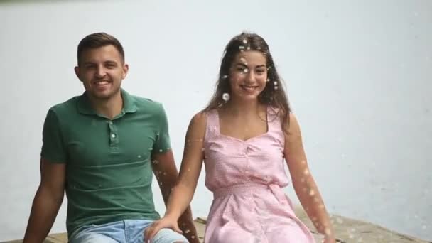 Beautiful youn couple sit on the pier near the lake. make splash by feet. slow motion — Stock Video