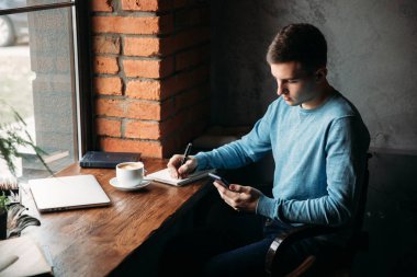 Genç bir iş çalışan ve bir kafede kahve içme ve not defterinde bir şey yazmak