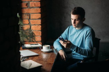 Yakışıklı çocuk kafede kahve içme. Pencerenin laptop ve defter ile oturuyor