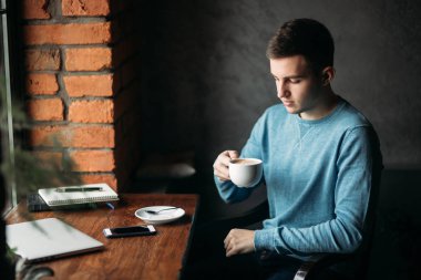 Yakışıklı çocuk kafede kahve içme. Pencerenin laptop ve defter ile oturuyor